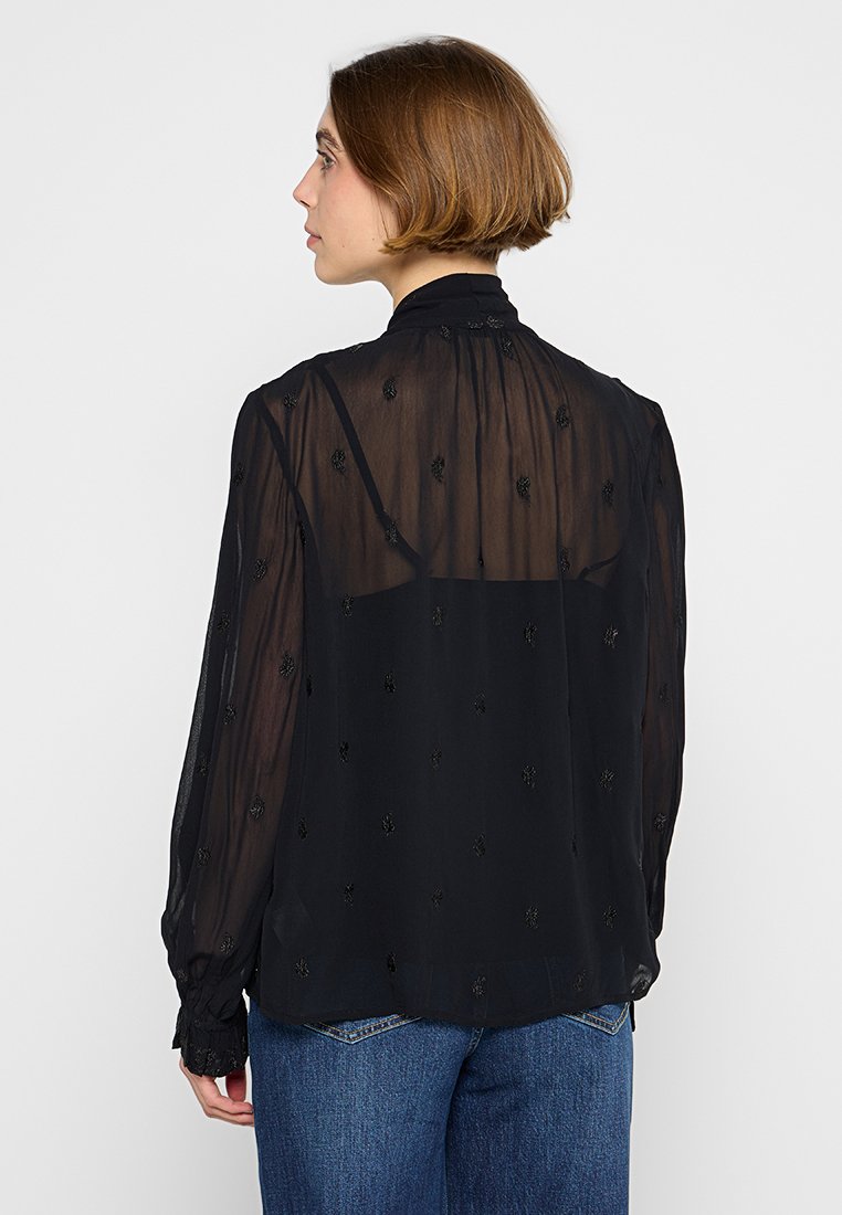 Schwarze transparente Bluse mit langen Ärmeln, floraler Stickerei, hohem Kragen und gerafften Manschetten. Tragen Sie sie zu blauen hochtaillierten Jeans.