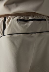 Beige byxor med svarta detaljer, med en mjuk textur och elastisk midja. Inkluderar en bakficka med dragkedja för säker förvaring.