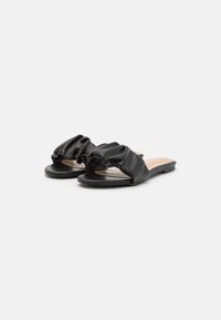 Sandali piatti neri con tomaia in ecopelle morbida e arricciata e design open toe. Presentano un sottopiede liscio e una suola in gomma minimalista.