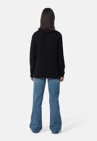 Svart texturerad tröja med långa ärmar, matchad med ljusblå utsvängda jeans. Tröjan har en rundad halsringning och sidofliser.