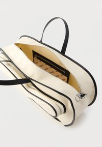 Torba z płótna z czarną lamówką, dwoma zamykanymi na zamek kieszeniami oraz wnętrzem wyłożonym tkaniną. Posiada krótkie czarne uchwyty i usztywniony kształt.