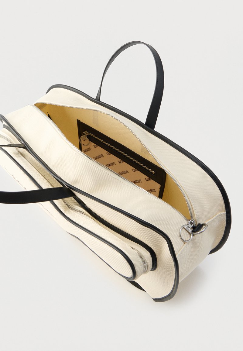 Canvas-Tasche mit schwarzem Rand, zwei Reißverschlussfächern und einem innen mit Stoff ausgekleideten Innenraum. Verfügt über kurze schwarze Griffe und eine strukturierte Form.