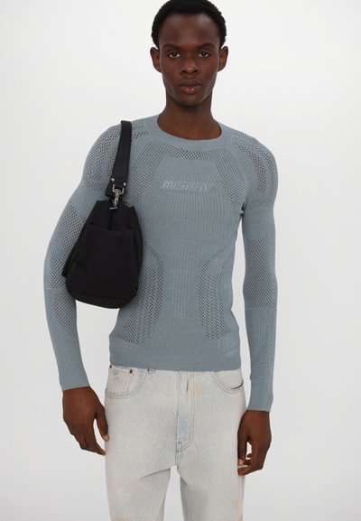 Fijngebreide lichtblauwe trui met netstructuur, met lange mouwen en een paarse logo. Gepaard met een zwarte schoudertas.