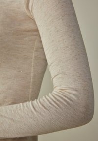 Světle béžová košile s dlouhým rukávem a texturovaným povrchem, která obsahuje jemné třpytivé vlákna rozprostřená po látce a má přiléhavý střih.