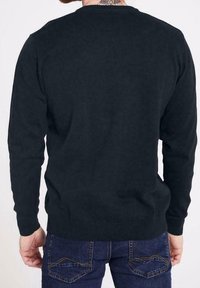 Maglione a coste grigio scuro con scollatura rotonda, maniche lunghe e orlo aderente, indossato da una persona di spalle, abbinato a jeans blu.