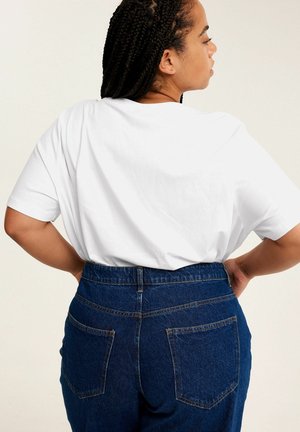 Weißes Baumwoll-T-Shirt mit kurzen Ärmeln, kombiniert mit hoch taillierten blauen Jeans aus Denim, die zwei Gesäßtaschen und abgesteppten Nähten aufweisen.