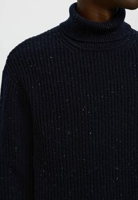 Suéter de cuello alto tejido en azul marino oscuro con una textura de canalé y motas multicolores. Presenta un collar alto y un diseño de corte holgado.