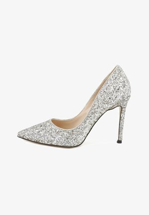 Chaussure à talon haut pointu couverte de paillettes argentées avec talon stiletto et doublure intérieure beige sur fond blanc.