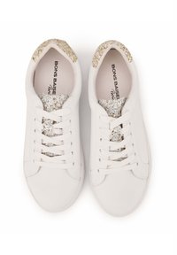 Des baskets blanches avec un extérieur en cuir lisse, des accents dorés pailletés sur le talon et la languette, et des lacets plats. Semelle intérieure texturée visible.