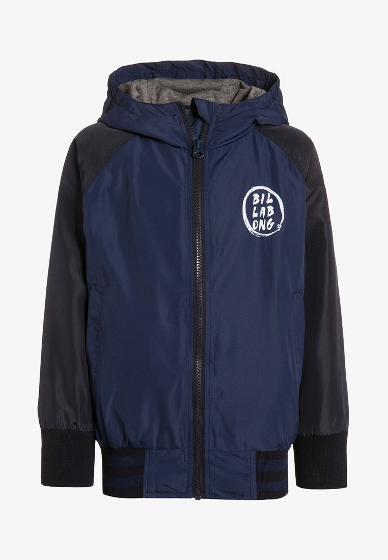 Granatowa kurtka przeciwwiatrowa z szarym podszewką, z zapięciem na zamek, kapturem i białym logo na klatce piersiowej. Czarny akcent na ramionach i mankietach.