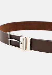 Cintura in pelle marrone con una finitura liscia, caratterizzata da una fibbia e un accento in metallo argentato, progettata per una vestibilità regolabile.