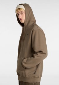 Brauner Hoodie mit einer Fronttasche, Kordelzugkapuze und gerippten Details. Robustes Material mit einer glatten Textur. Dezentes Logo auf der Brust.