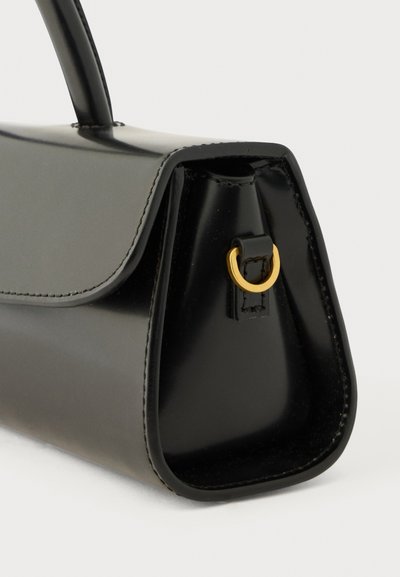 Čierna kožená kabelka s pevnou, trapezoidnou skladbou, hornou rúčkou a malým zlatým D-krúžkom na bočnom paneli.