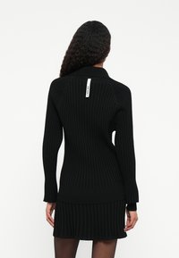 Abito a coste nere con colletto, maniche lunghe e etichetta posteriore. Il design presenta texture a contrasto e una silhouette aderente.