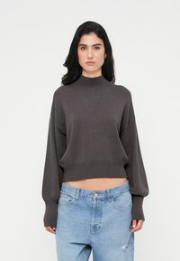 Κοντή, σκούρα γκρι μπλούζα με λαιμόκοψη ψηλή και φαρδιά μανίκια. Συνδυασμένη με ανοιχτό μπλε, χαλαρά τζιν με φθαρμένες λεπτομέρειες.