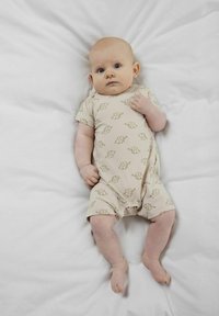 Beżowy body z krótkim rękawem, zdobione powtarzającym się wzorem słoni, z zapięciem na napy na dole, noszone przez niemowlę na białej powierzchni.