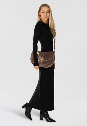 Borsa a spalla in suede marrone con una tracolla a catena dorata, dettaglio floreale ricamato e forma arrotondata, abbinata a un vestito nero a maniche lunghe.