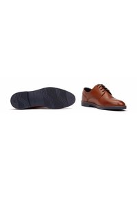 Chaussures de ville en cuir marron avec une finition lisse, bout rond, design à lacets, et semelle en caoutchouc noir avec un motif de crampons.