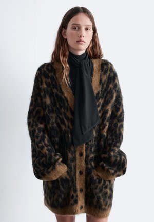Brown leopard print cardigan with black accents, fuzzy texture, oversized shape, and six button closure; worn over a black blouse with a scarf.