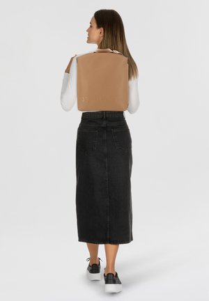Brauner Leder-Rucksack mit geprägtem Logo, rechteckiger Form und strukturiertem Oberflächenmaterial. Trägt eine Person mit einem schwarzen Denim-Rock auf dem Rücken.