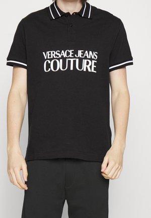 Sort polo-shirt med hvide stribe-accenter på kraven og ærmerne, med "VERSACE JEANS COUTURE"-logo i fed, hvid skrift.