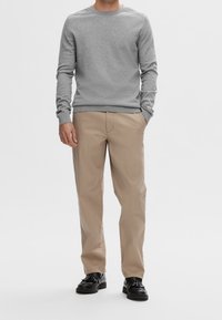 Pull gris à manches longues et col rond, associé à un pantalon beige à jambes droites, présentant une texture lisse et des chaussures noires avec un nœud en accent.