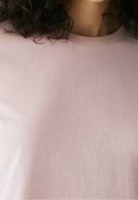 Top rosa chiaro a maniche corte realizzato in un tessuto morbido con una struttura liscia. Presenta un collo rotondo e un design semplice e casual.