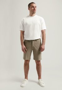 Tricou alb din bumbac, pantaloni scurți kaki și adidași albi. Tricoul are mâneci scurte; pantalonii scurți sunt de lungime până la genunchi și au un design simplu.