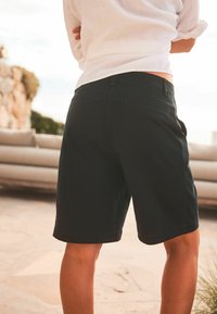 Shorts noirs en coton avec une texture lisse, de longueur genou, avec des détails de couture minimaux et des poches à l'arrière.