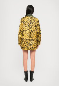 Giacca con stampa leopardata gialla e nera, colletto verde, maniche lunghe e vestibilità rilassata, dotata di bottoni e superficie leggermente texturizzata.