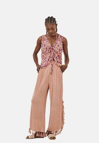 Conjunto de dos piezas que incluye una blusa sin mangas con un estampado floral en tonos rosa y púrpura, combinada con pantalones sueltos de color rosa claro con acentos de borlas.