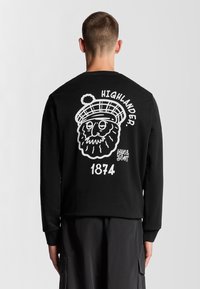 Felpa nera a maniche lunghe con un design grafico bianco che presenta un personaggio, il testo "HIGHLANDER" e "1874". I polsini a costine completano il look.