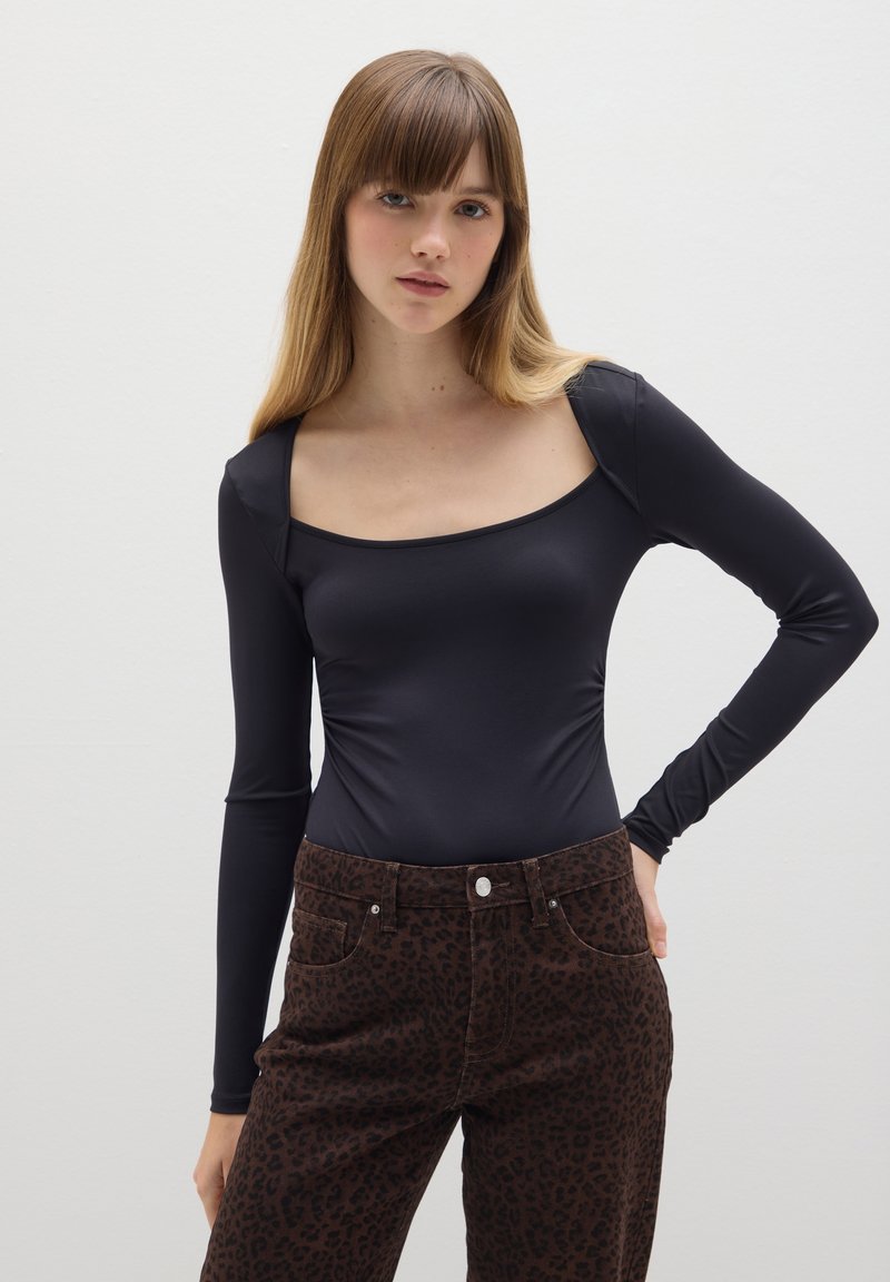 Body nero a maniche lunghe con scollatura quadrata, abbinato a pantaloni marrone con stampa leopardata, dotati di tasche e chiusura con bottone metallico.