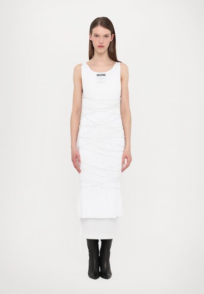 Rochie albă cu decolteu rotund și detalii intricate din frânghie albă, design stratificat și etichetă neagră; asortată cu cizme negre până la genunchi.