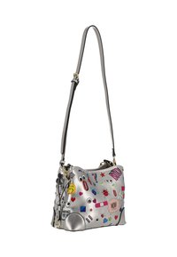 Srebrna torebka z ekoskóry z kolorowymi, kreskówkowymi naszywkami. Posiada odpinany pasek, zamknięcie na suwak oraz teksturowany akcent z boku.