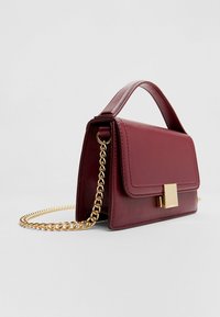 Burgunderfarbene Lederhandtasche mit strukturiertem Design, goldener Kettenriemen, Obergriff und vorderer Verschlussdetails. Glatte Oberfläche.