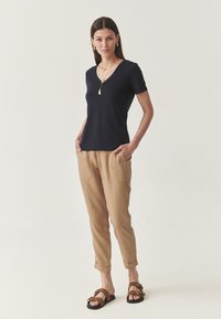 Marine V-hals T-shirt, beige loszittende broek met zijzakken, en bruine sandalen met dubbele banden en gespen. Hèque textuur, casual stijl.