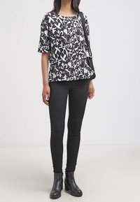 Top corto a maniche corte in bianco e nero con un motivo di testo astratto, abbinato a leggings neri aderenti e stivali alla caviglia, con una borsa.