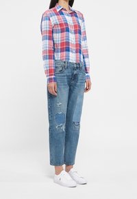 Plaid button-up shirt in red, blue, and white; paired with distressed light blue jeans featuring patches; worn with white sneakers.