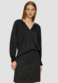Black silk blouse with a V-neck, pleated long sleeves, and a relaxed fit, paired with a textured black skirt featuring metallic accents.