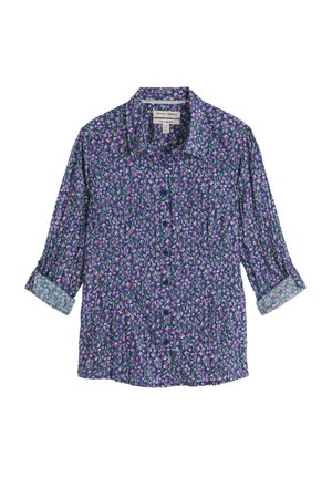 Kukkakuvioinen nappipaita, jonka pohjaväri on sinivioletti ja jossa on pieniä vaaleanpunaisia ja vihreitä kukkakuvioita. Pitkät hihat on kääritty, ja niissä on vaaleansininen yksityiskohta.