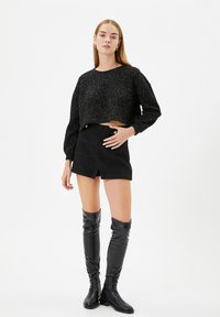 Czarny krótki sweter z metalicznymi akcentami, w połączeniu z czarną krótką spódnicą z złotymi guzikami. Czarne skórzane kozaki do kolan.