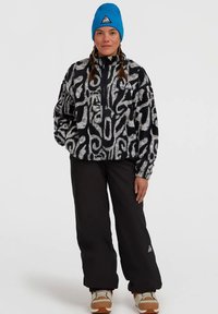 Fuzzy black and white pullover jacket with a quarter-length zipper and side pockets. Paired with black pants and a bright blue beanie.