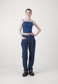 Džínová crop top s tenkými ramienkami; vysoko pásové, voľné tmavé džínsy; robustné čierne platformové topánky s fialovými akcentmi.