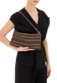 Borsa a tracolla a strisce marroni con una superficie testurizzata e cuciture a contrasto, tenuta contro un indumento nero.