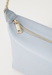 Borsa in pelle blu chiaro con una zip dorata e una catena. Tessuto liscio, design minimalista con una lucentezza sottile e cuciture pulite.