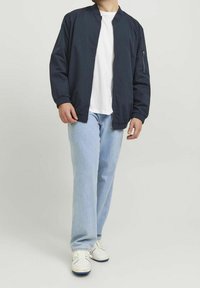 Marinblå bomberjacka med en ficka med blixtlås, kombinerad med en vit t-shirt och ljusblå jeans, bärs med vita sneakers.