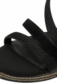Mustmustel mustratest, sametilaadne ülemine osa ja tekstureeritud jalatugi loodusliku kudumise detailiga servas.