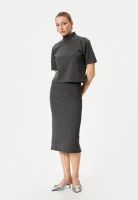 Grå ribbet strik sæt bestående af en cropped top med korte ærmer og høj hals, suppleret med en knælængde blyantskørt. Sølvfarvede sko.