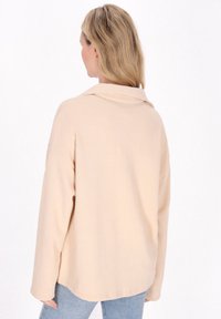 Beige csíkozott, hosszú ujjú felső, galléros nyakkal és leengedett vállakkal, világoskék farmernadrággal párosítva. Sima textúra és laza fit.
